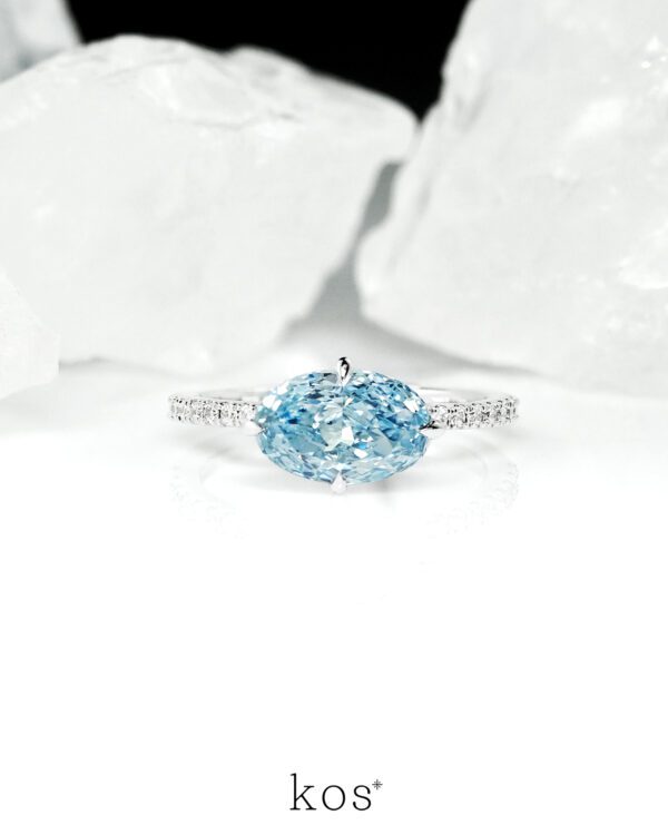 แหวนหมั้นเพชร Oval สีฟ้าทรง วางแนวนอน (East-West) บนตัวเรือนทองคำขาวฝังเพชร ดีไซน์แบรนด์ kos