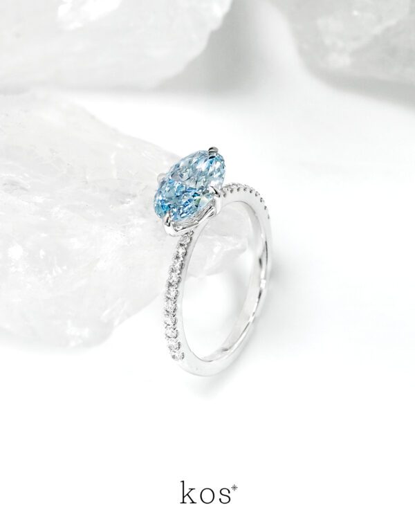 แหวนหมั้นเพชร Oval สีฟ้าทรง วางแนวนอน (East-West) บนตัวเรือนทองคำขาวฝังเพชร ดีไซน์แบรนด์ kos