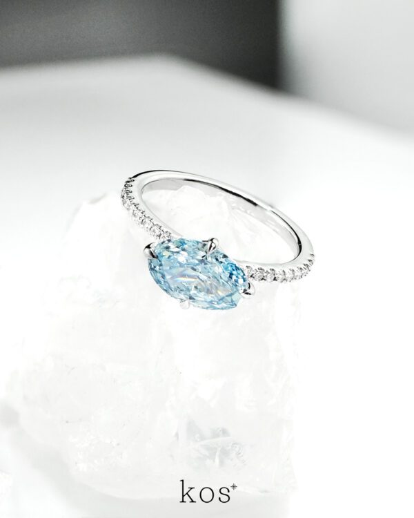 แหวนหมั้นเพชร Oval สีฟ้าทรง วางแนวนอน (East-West) บนตัวเรือนทองคำขาวฝังเพชร ดีไซน์แบรนด์ kos